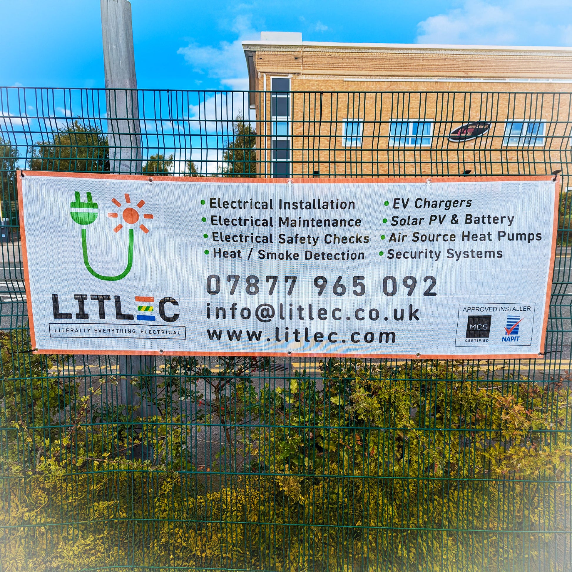 A printed mesh banner hanging from a green railed fence. Litlec branding, printed by Kraken Signs.